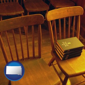 wooden chairs and hymnals in an old church building - with South Dakota icon